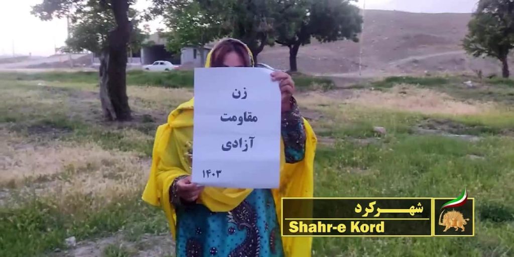 إحدى عضوات في وحدات المقاومة التابعة لمجاهدي خلق الإيرانية في مدينة شهركرد ترفع في يده لوحة بعنوان "المرأة، المقاومة، الحرية".